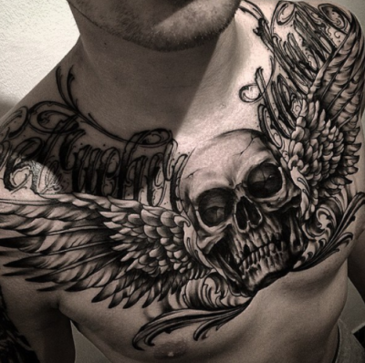 Татуировка с черепом крыльями и надписями на груди у мужика