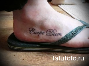 Фото тату с надписью 'Carpe Diem' на стопе. Красный цвет, каллиграфический шрифт, минималистичный стиль, вдохновляющая фраза.