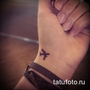 Фото тату маленького черного самолетика на женском запястье. Минималистичный рисунок татуировки для любителей путешествий.