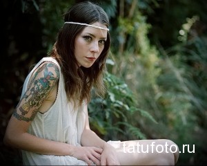 Фото тату: девушка с татуировкой в стиле чикано на руке. Изображены религиозные мотивы, цветы и надписи.