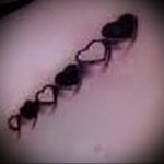 Фото тату цепочки из маленьких черных сердечек на коже, выполненное в минималистичном стиле с тонкими линиями.