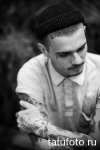 Фото тату на лице и руках мужчины: геометрические узоры и надписи в стиле blackwork. Черные татуировки на лбу, щеках и руках.