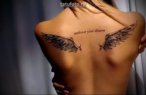 Фото тату двух небольших крыльев ангела на спине с надписью 'embrace your dreams' в черно-серых тонах.