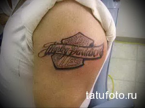 Фото тату логотипа Harley-Davidson на плече. Классический дизайн в черно-белых тонах.