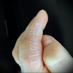 Фотография татуировки надписи "I Love Him" на пальце руки. Белый цвет, каллиграфический шрифт.