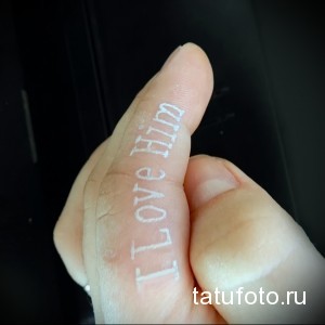 Фотография татуировки надписи "I Love Him" на пальце руки. Белый цвет, каллиграфический шрифт.