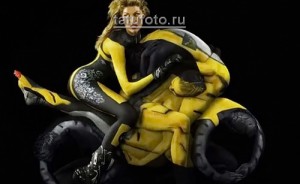 Фото боди-арта: двое людей, раскрашенные в желтый и черный цвета, изображают мотоцикл с водителем и пассажиром. Динамичный и креативный рисунок.