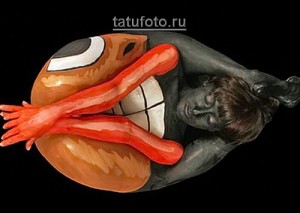 Фото тату: сюрреалистичный рисунок, изображающий человека, застрявшего в пасти огромной рыбы, выполненный в ярких цветах.