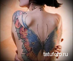 Фото тату бабочки на спине девушки. Яркая, красочная татуировка с детально проработанными крыльями и цветочными элементами.