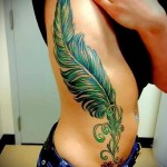 большое перо зеленого цвета - женская татуировка на боку