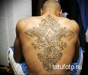 Фото татуировки на спине мужчины: большой крест с надписями 'I SHALL FEAR GOD' и 'FEAR NO MAN'. Детализированный рисунок в коричневых тонах.