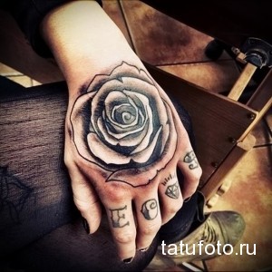 Фотография татуировки большой реалистичной розы на руке. Черно-серые тона, детальная проработка лепестков и листьев.