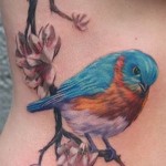 ветка цветов и маленькая цветная птичка - женская татуировка на боку