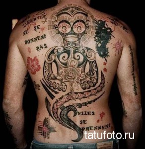 Фото тату на спине с изображением абстрактной композиции, включающей геометрические фигуры, символы и надписи на французском языке. Рисунок выполнен в различных стилях и техниках.