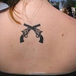 два скрещенных пистолета на спине у девушки сзади - фото татуировки