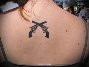 Фото тату двух скрещенных пистолетов на спине женщины. Простой черно-белый рисунок.