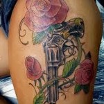 женская тату с револьвером и цветами роз на ногу сбоку
