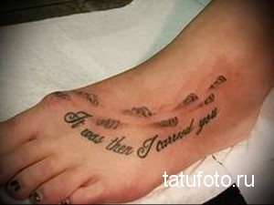 Фотография татуировки на стопе с надписью 'It was then I carried you', выполненной каллиграфическим шрифтом. Татуировка выполнена в коричневых тонах.