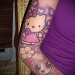 Фото тату: яркая и красочная татуировка с изображением Hello Kitty, Powerpuff Girls и цветов на руке девушки. Мультяшный рисунок татуировки.