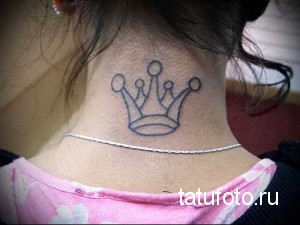 Фото тату простой короны на задней части шеи девушки. Эскиз татуировки выполнен в минималистичном стиле с тонкими линиями.