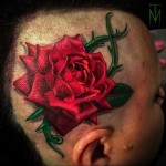 красная роза с шипами в женской татуировке на голове
