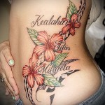 красные цветы и надпись - женская татуировка на боку