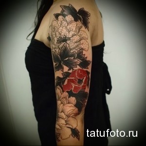 Фото тату: Женская рука с татуировкой, изображающей букет пионов в черно-белой гамме с добавлением красного цвета. Детализированное и элегантное изображение.