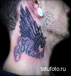 Фото тату крыла и надписи 'Blessed' на шее мужчины. Черно-белая татуировка в готическом стиле.