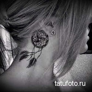 Черно-белое фото тату ловца снов на затылке девушки. Детализированный рисунок с перьями и паутиной, выполненный в графическом стиле.