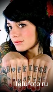 Фото тату на пальцах: надпись "Hopeless Romantic" выполненная в стиле олдскул. Цветная татуировка, шрифт с засечками.