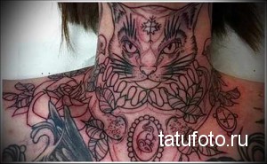 Фото татуировки с изображением головы кошки на шее, переходящей в узоры на спине. Яркий рисунок с использованием черных и розовых тонов.