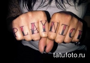 Фото тату: надпись 'PLAY NITCH' на костяшках пальцев рук, выполненная в стиле олдскул с использованием красного и черного цветов.