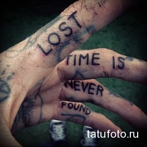 Фото татуировки с надписью "Lost time is never found" на пальцах рук. Черный цвет, готический шрифт, философский смысл.