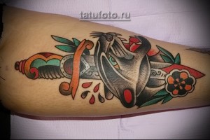 Фото тату на предплечье: голова пантеры, пронзенная кинжалом, выполнена в стиле олд скул с использованием ярких цветов и традиционных элементов.