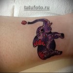 Фото тату слоненка с розовым лотосом на запястье. Нежные пастельные тона, мультяшный стиль, женственная татуировка.