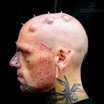 Фото тату на шее и лице: красная бабочка, выполненная в стиле трайбл, на фоне модификаций кожи.