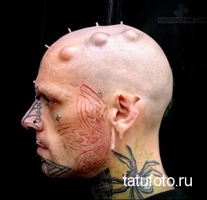 Фото тату на шее и лице: красная бабочка, выполненная в стиле трайбл, на фоне модификаций кожи.
