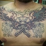 пистолеты, костет, крылья и надписи в большой татуировке на груди мужчины