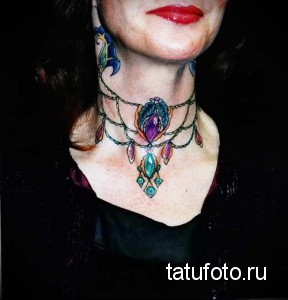 Фото тату, имитирующего колье на шее и груди. Татуировка выполнена в ярких цветах с использованием драгоценных камней и изящных линий.