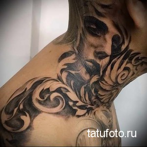 Фото тату черепа с узорами на шее. Татуировка выполнена в черно-серых тонах с использованием техники светотени для создания объемного эффекта.