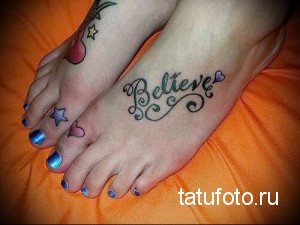 Фотография татуировки на стопе с надписью 'Believe', выполненной каллиграфическим шрифтом и украшенной сердечком. Татуировка выполнена в черных тонах.