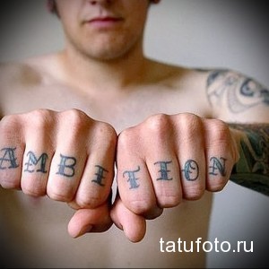 Фото татуировки с надписью 'AMBITION' на костяшках пальцев. Черные чернила, минималистичный стиль, мужская рука.