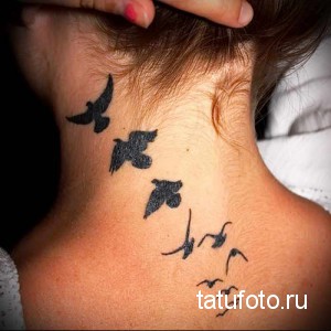 Фото тату стаи летящих птиц на шее. Татуировка выполнена в черном цвете с минималистичным дизайном и акцентом на динамику полета.