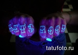 Фотография татуировок надписей "LET'S ROCK" на пальцах рук, светящихся в ультрафиолетовом свете. Неоновый эффект, оригинальный дизайн.