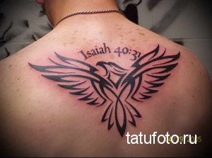 Фото тату: Черно-белая татуировка птицы в полете с библейской цитатой "Isaiah 40:31" на спине мужчины, выполненная в минималистичном стиле.