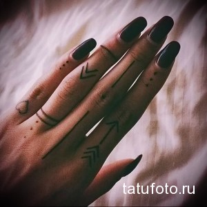 Фотография женской руки с татуировками геометрических стрел и линий. Минималистичные татуировки черным цветом.