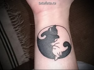 Фото тату Инь и Ян с изображением черного и белого котенка внутри символа. Татуировка выполнена на запястье.