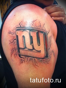 Фото татуировки с логотипом команды New York Giants на плече. Синий, красный и белый цвета, трещины.