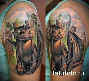 Фото тату Ночной Фурии (Toothless) из мультфильма "Как приручить дракона" на плече. Цветная татуировка с детально прорисованными элементами.