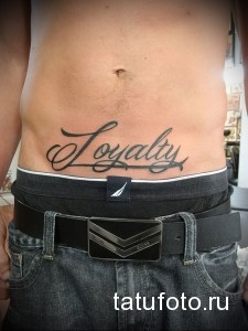 Фото тату надписи 'Loyalty' красивым курсивом на животе мужчины.